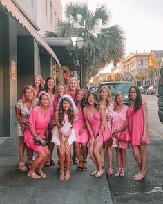 a group of women in pink dresses posing for a photo on the sidewalk near a building