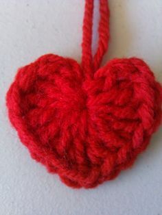 a crocheted red heart ornament hanging from a string on a white surface