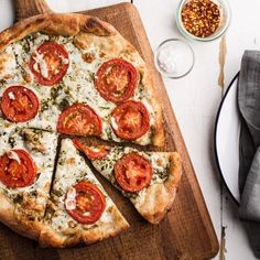 a pizza on a cutting board with slices taken out of it and other ingredients nearby