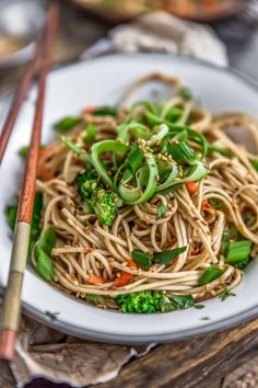 a white plate topped with noodles and veggies next to two chopsticks