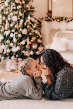 a mother and her daughter laying on the floor in front of a christmas tree