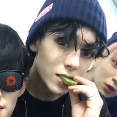 three young men with sunglasses and beanies are eating some food while looking at their cell phones