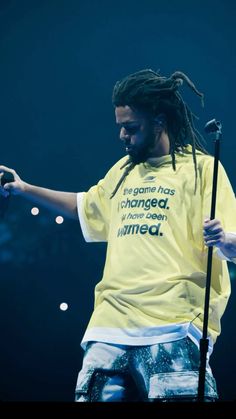 a man with dreadlocks on his head holding a microphone and wearing a yellow shirt