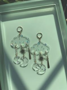 two key chains with charms attached to them on a white tray in front of a window