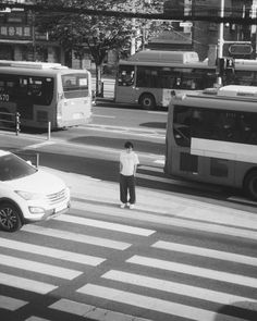 a man standing in the middle of a crosswalk with buses and cars behind him