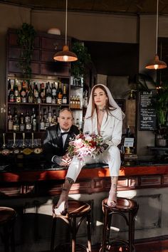 a woman sitting on top of a bar next to a man in a tuxedo