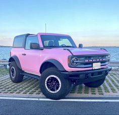 a pink pick up truck parked on the side of the road next to water and grass