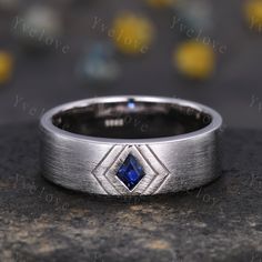 a white gold wedding band with a blue sapphire stone in the center, on a granite surface