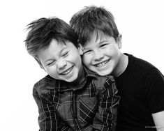 two young boys are hugging each other and smiling at the camera, black and white