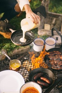 a person pouring sauce over hot dogs on a grill