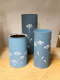 three blue vases sitting on top of a wooden table with flowers painted on them