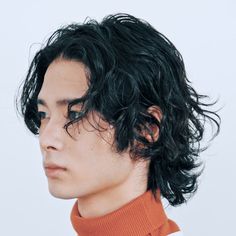 a man with black hair and an orange turtle neck sweater looking off to the side