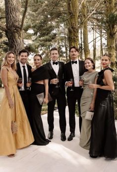 a group of people standing next to each other in formal wear and holding wine glasses