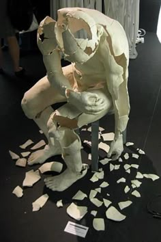 a white sculpture sitting on top of a chair covered in pieces of torn up paper