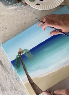 someone is painting a palm tree on the beach with watercolors and paper plates