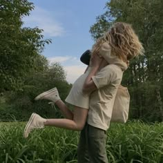 a man and woman are hugging in the middle of tall grass with trees behind them