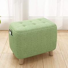 a small green ottoman sitting on top of a hard wood floor next to a potted plant