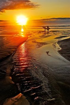 two people are walking on the beach at sunset