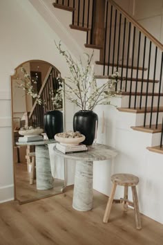 a table with two vases on it in front of a mirror and stairs leading up to the second floor