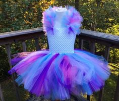 a purple and blue tutu dress sitting on top of a wooden rail next to trees