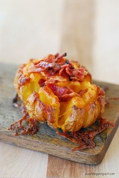 a baked potato covered in bacon sitting on top of a wooden cutting board