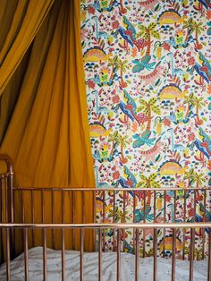 a baby crib in front of a colorful wallpaper and drapes with gold metal rails