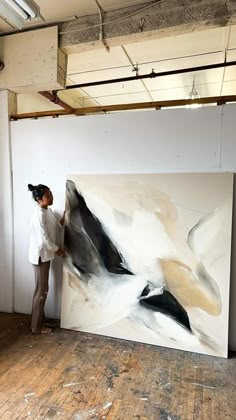 a woman standing next to a large painting in an art studio with wooden floors and exposed ceilings