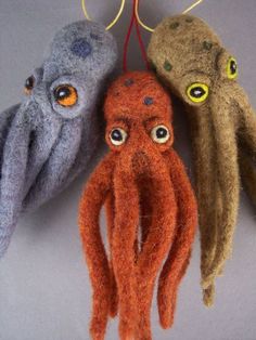 three stuffed animals hanging from strings on a gray surface with yellow eyes and one orange octopus