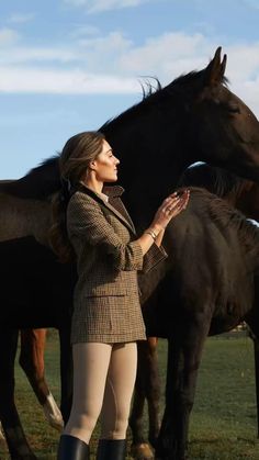 a woman standing next to two horses in a field with one holding her hand out