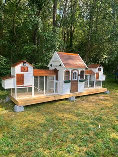 a small white chicken coop in the middle of a grassy area with trees behind it