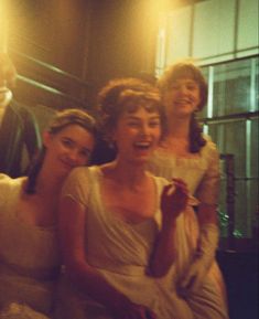 three women in white dresses sitting next to each other and one woman is smiling at the camera