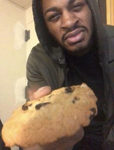 a man in a black hoodie is holding a piece of bread with chocolate chips on it