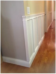 an empty hallway with hard wood flooring and white paneling on the side wall