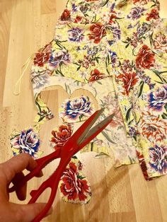 someone is cutting out fabric with scissors on a wooden floor next to them and another pair of red handled scissor