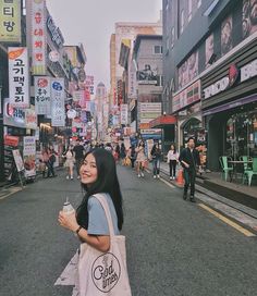 a woman standing on the side of a street holding a drink in her hand and smiling