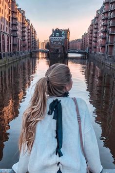 a woman sitting on the edge of a bridge looking down at water and buildings in the background