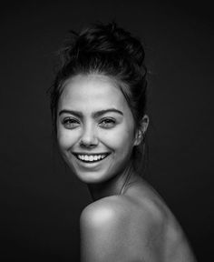 a black and white photo of a young woman smiling at the camera with her hair in a bun