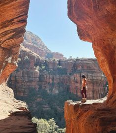 a man standing on top of a cliff next to a canyon filled with trees and rocks