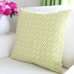 a green pillow sitting on top of a white couch next to a vase with pink flowers