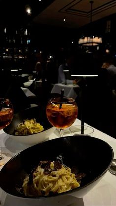 two glasses of wine sit on a table with food and drinks in front of them