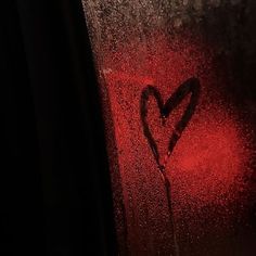 a heart drawn on a window with rain drops and red light coming from behind it