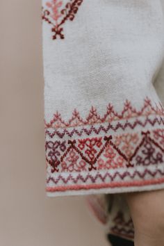 a woman's hand holding up a white and red patterned piece of cloth that has been stitched together