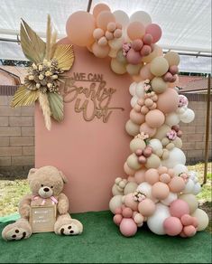 a teddy bear sitting next to a giant balloon arch with balloons on it's sides