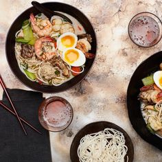 two black bowls filled with noodles and shrimp next to chopsticks on a table