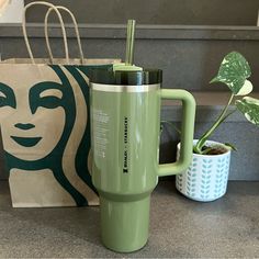 a green coffee cup sitting next to a starbucks bag and a plant in a vase