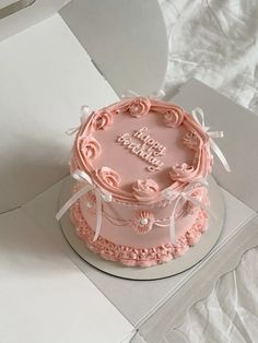 a pink birthday cake sitting on top of a white tablecloth covered box with the words happy birthday written in frosting