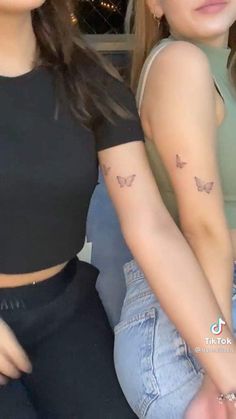 two young women sitting next to each other with small tattoos on their arms and shoulder