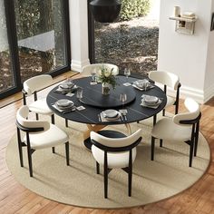 a dining room table with white chairs and a round rug in front of the window