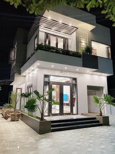 a modern house is lit up at night with plants on the balcony and stairs leading to the second floor