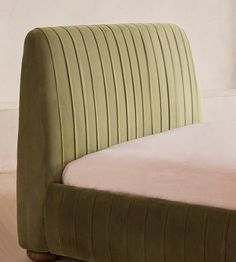 a bed with a green headboard sitting on top of a wooden floor